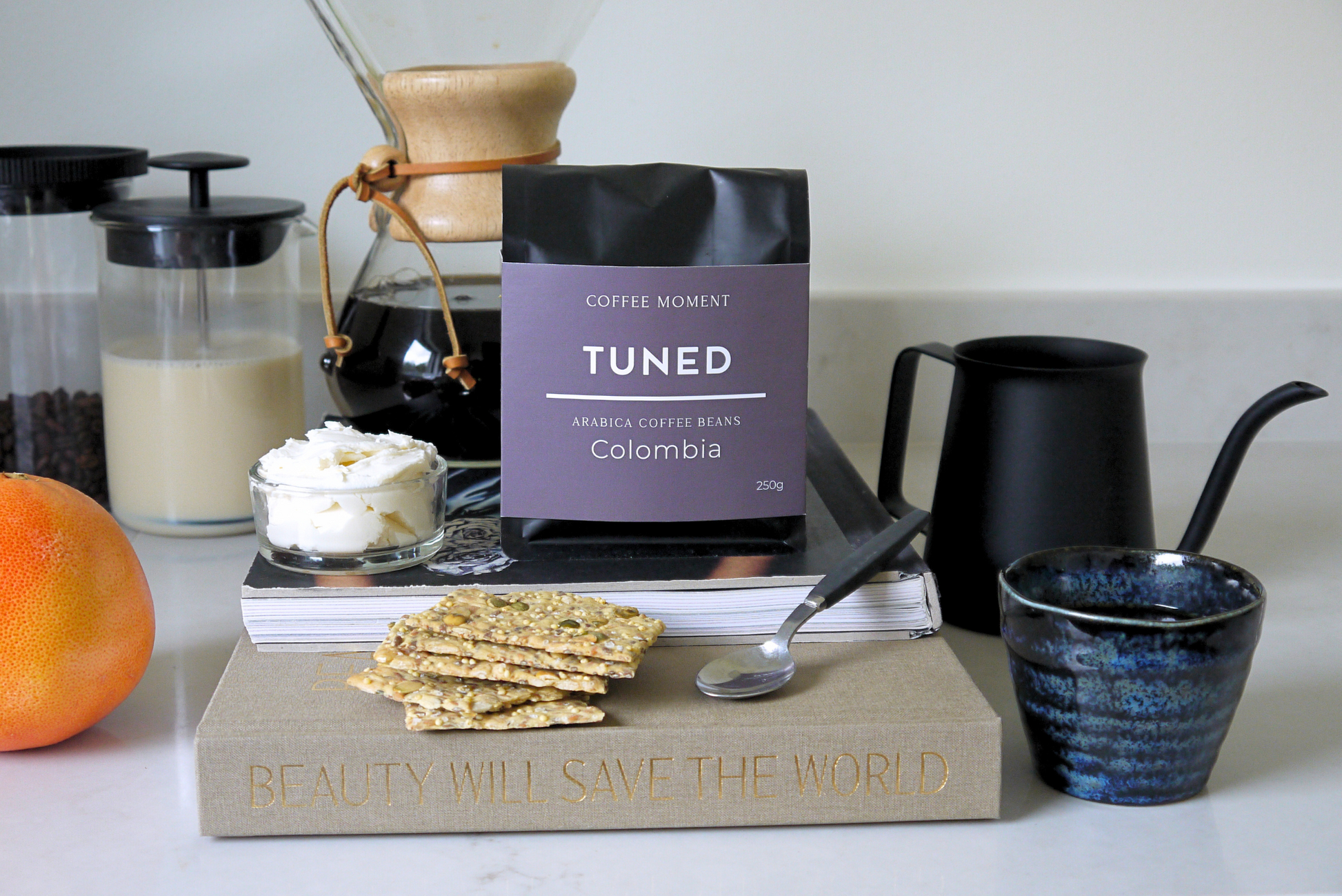 Coffee beans package labeled 'Tuned' on a table with coffee-making equipment and snacks.